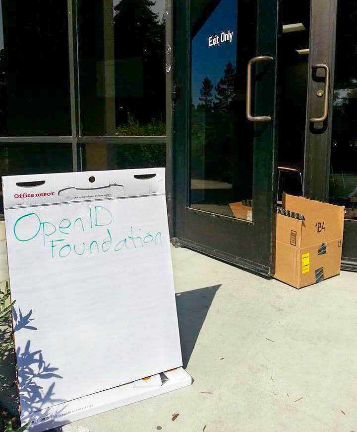 Picture of a sign reading OpenID Foundation in front of a door being propped open with a box.